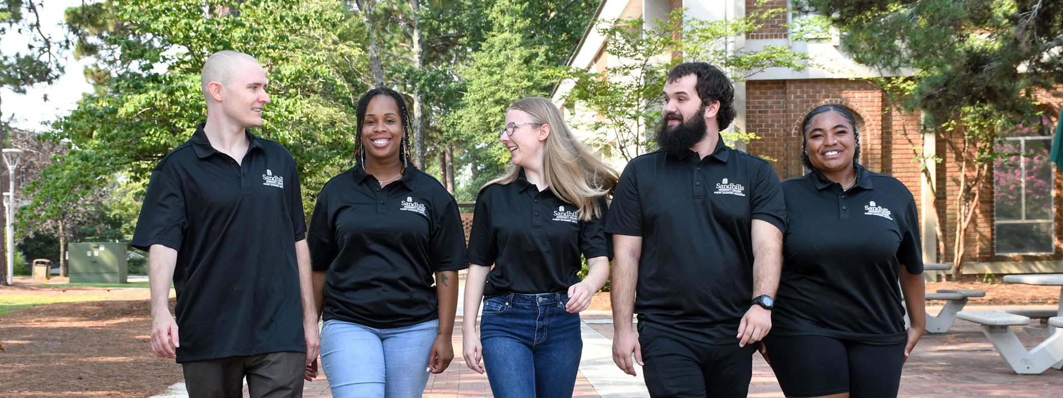 Five Student Government Association members walk together along a brick pathway on the Sandhills Community College campus.