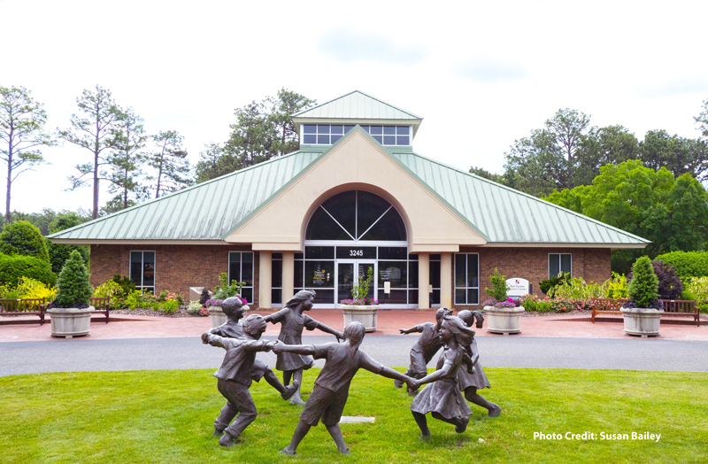 The Sandhills Horticultural Gardens Visitor Center with the Dancing Ring sculpture in the foreground and landscaped gardens surrounding the entrance.