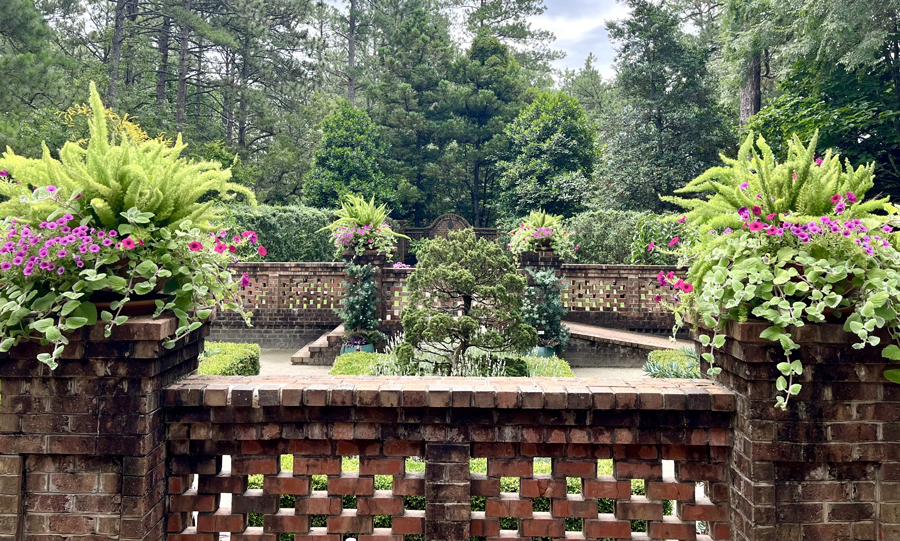 Brick terrace and planters filled with ferns and pink flowers overlooking the Sir Walter Raleigh Garden at Sandhills Horticultural Gardens.