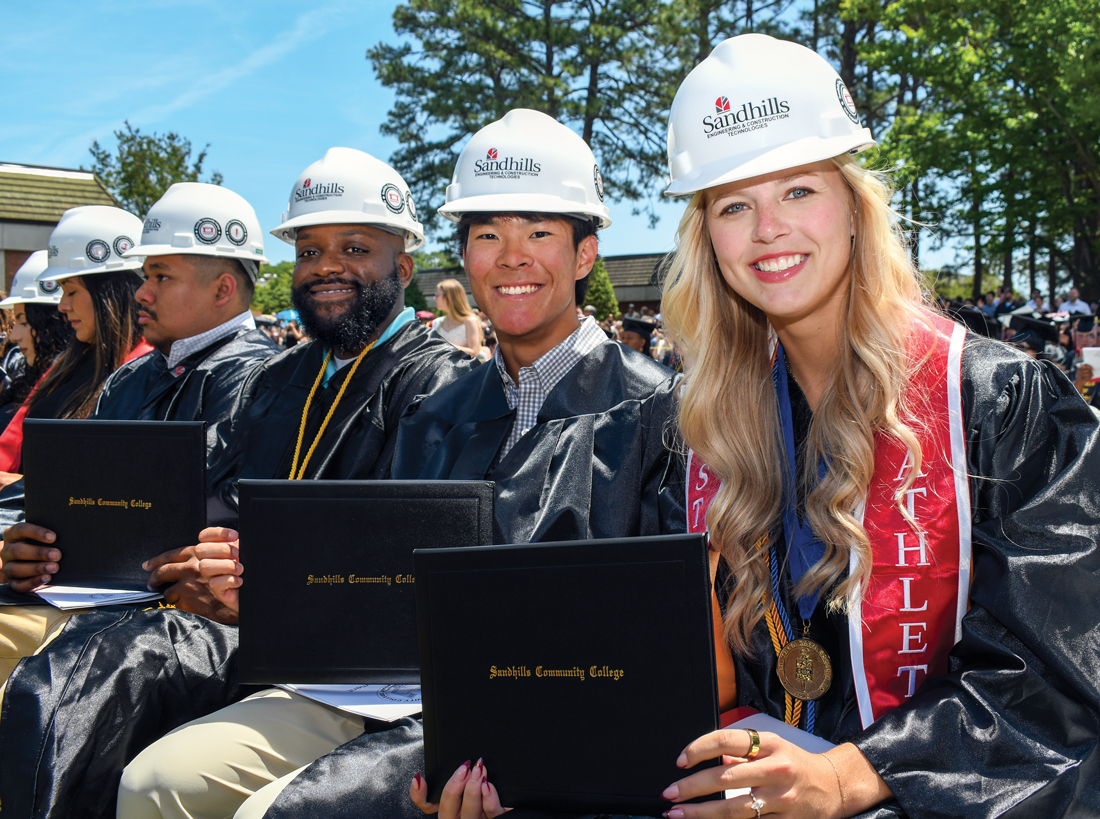 Sandhills Community College Graduates Celebrate Career Pathways Sandhills Community College graduates wearing Engineering and Construction Technologies hard hats and graduation regalia celebrate commencement while holding their diplomas.