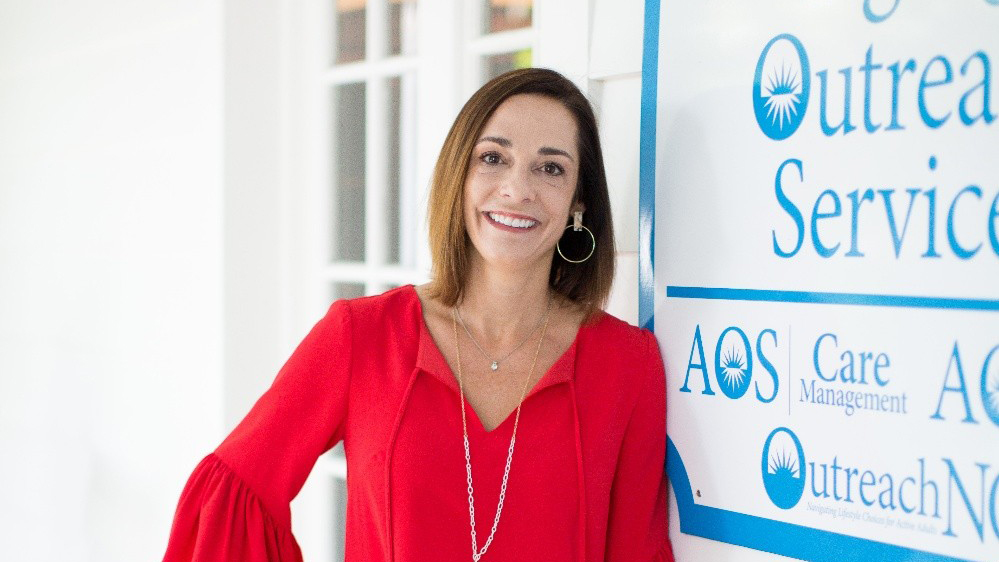 Amy Natt, founder of Aging Outreach Services, standing beside the organization’s signage.