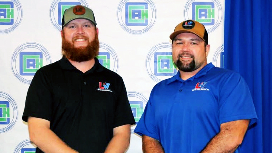 Tyler Lewis and Chris Wright of L&W Mechanical LLC stand side by side in branded polos and caps in front of a Raeford-Hoke Chamber backdrop at a business recognition event.