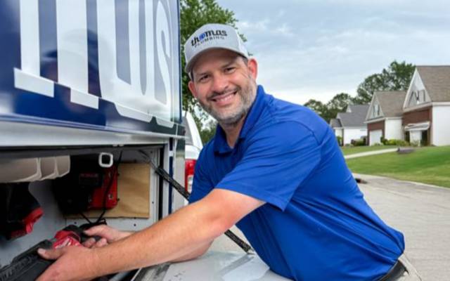 Thomas Plumbing technician retrieving tools from a company service truck while preparing for a residential plumbing service call.