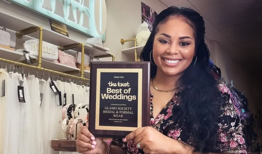 Kenna Parks holds a Best of Weddings award inside Glamo Society Bridal & Formal Wear.