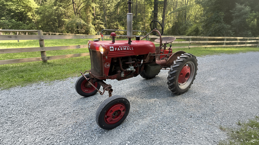 Vintage Farmall Cub tractor parked on a gravel drive beside a wooden fence.