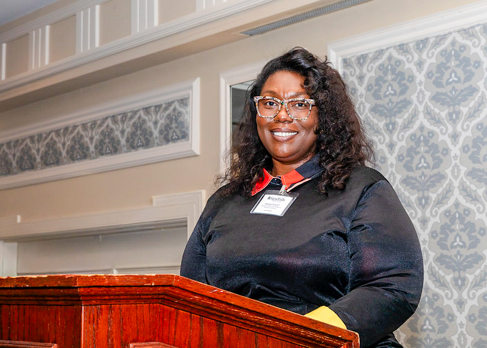 A student speaker stands at a podium labeled “Sandhills Community College,” smiling as she addresses attendees at the scholarship award dinner.
