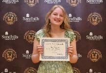 Abigail Kirkham – Student Awards Day Student Abigail Kirkham holding an award certificate and smiling in front of a Sandhills Community College Student Awards Day backdrop.