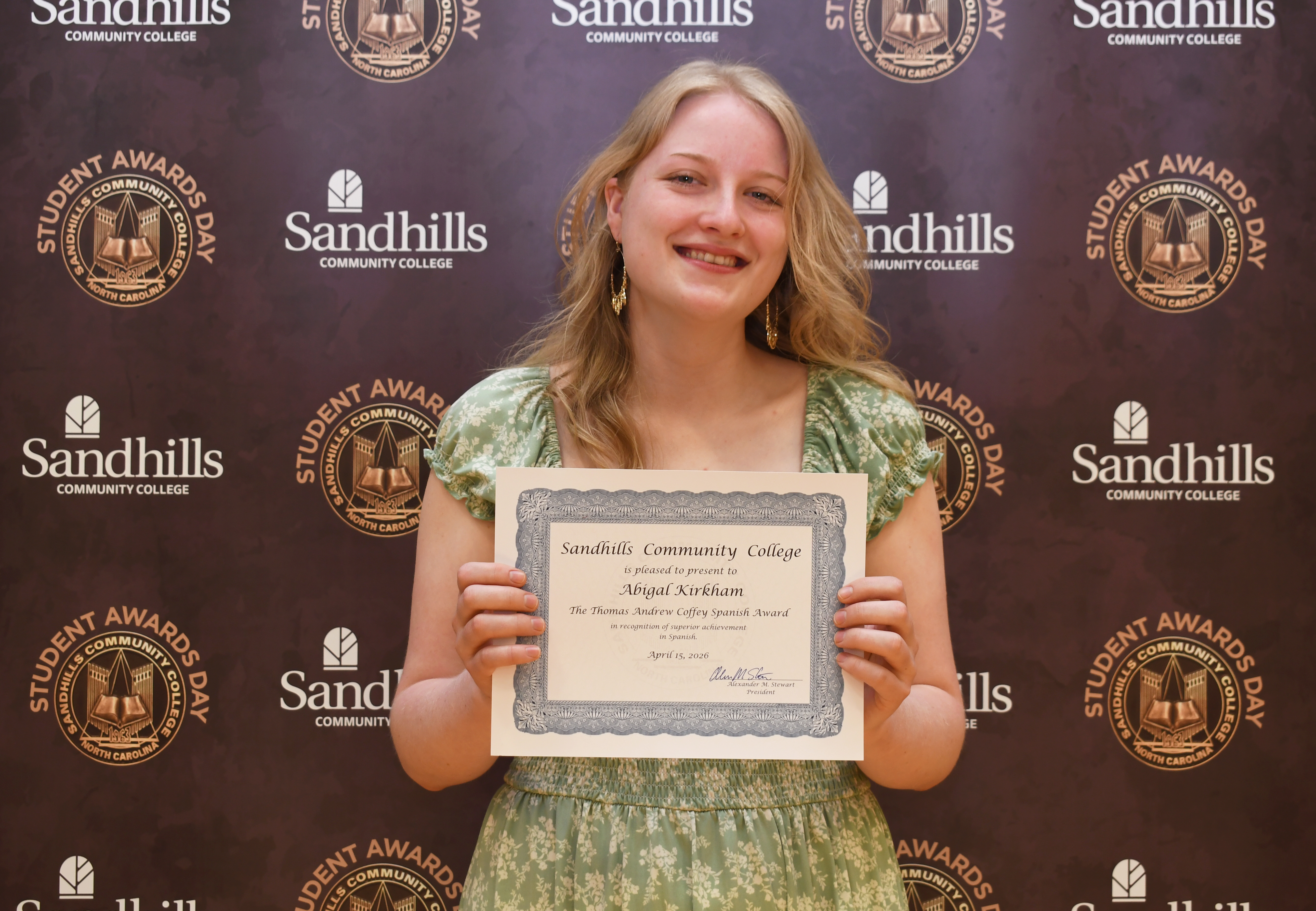 Student Abigail Kirkham holding an award certificate and smiling in front of a Sandhills Community College Student Awards Day backdrop.