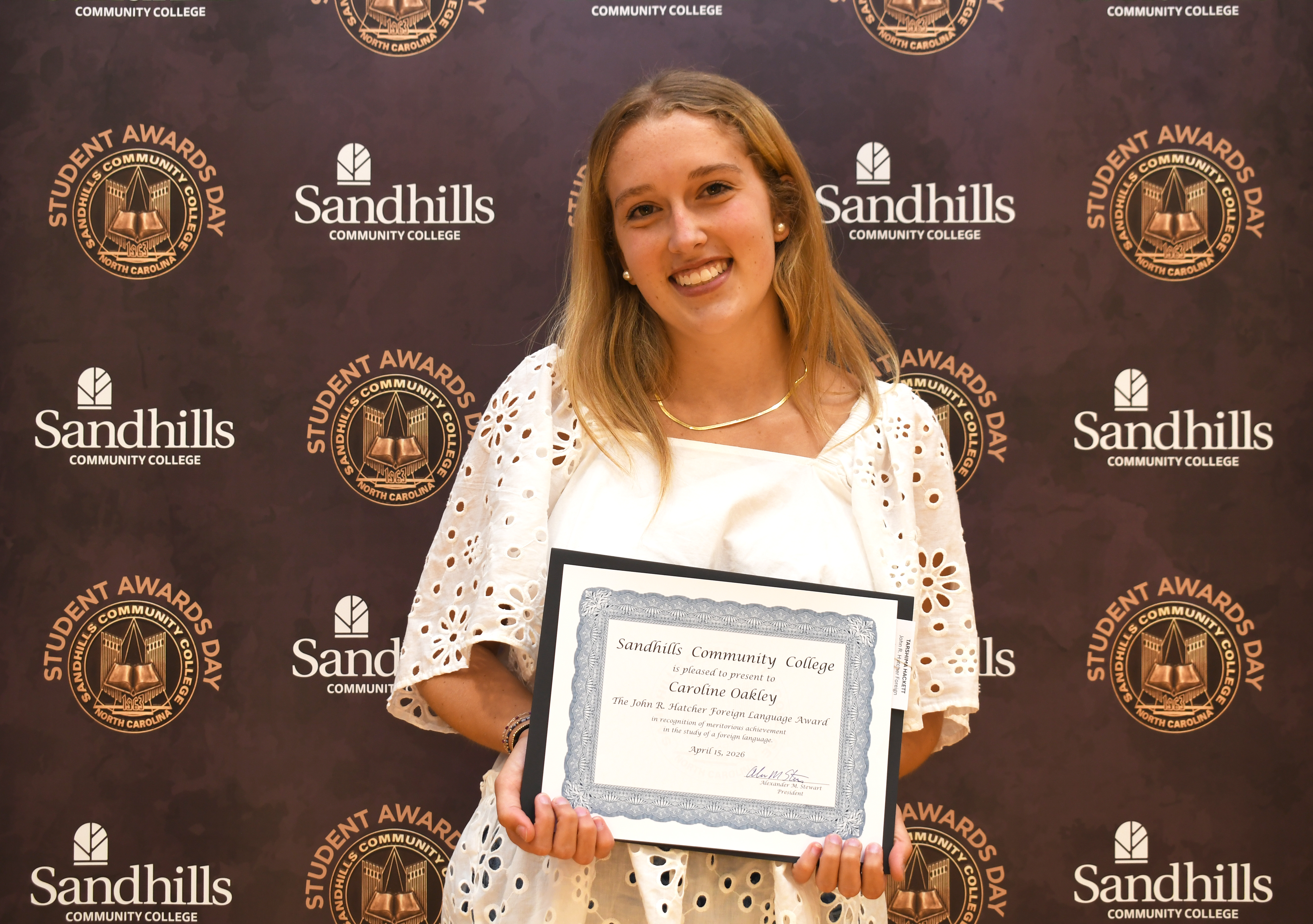 Student Caroline Oakley smiling and holding an award certificate in front of a Sandhills Community College Student Awards Day backdrop.