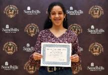 Danely Maldanado – Student Awards Day Student Danely Maldanado holding an award certificate and smiling in front of a Sandhills Community College Student Awards Day backdrop.