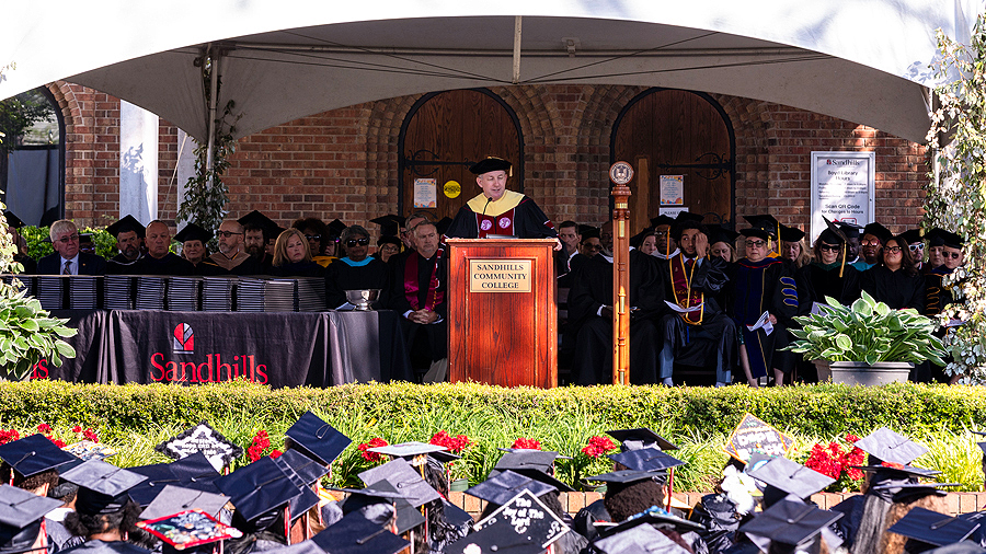 Sandhills Community College President Alexander “Sandy” Stewart speaking at the podium during the 2026 commencement ceremony as graduates, faculty, and guests look on.