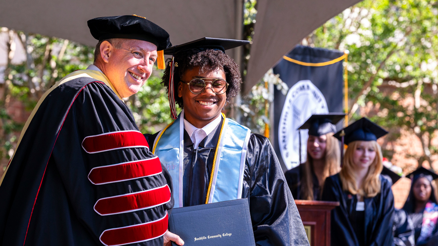 Sandhills Community College President Alexander “Sandy” Stewart posing with a smiling graduate in cap and gown during the 2026 commencement ceremony.