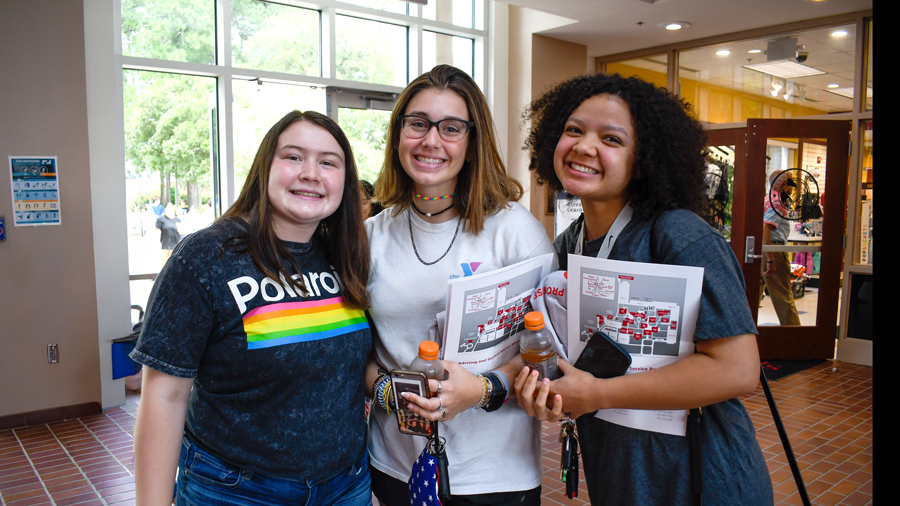 Three students smile while holding orientation materials during a New Student Orientation event inside Dempsey Student Center at Sandhills Community College.