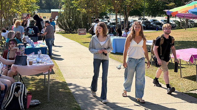 Students walk along a campus sidewalk past tables and displays during an outdoor student activity fair.