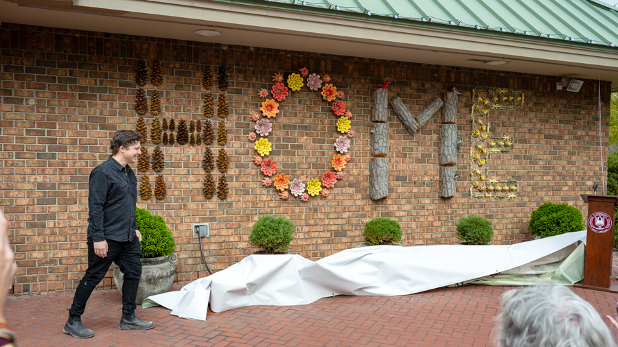 Artist Luke Huling walks beside his newly unveiled HOME art installation, featuring letters made from pine cones, colorful flowers and other natural materials.