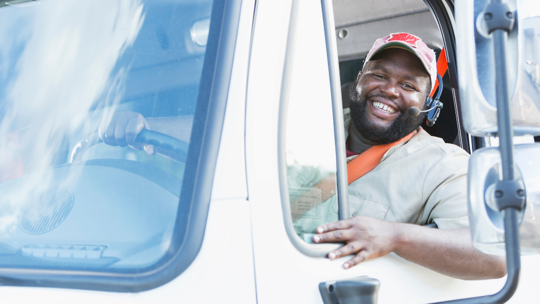 A truck driver is smiling out of his truck window.