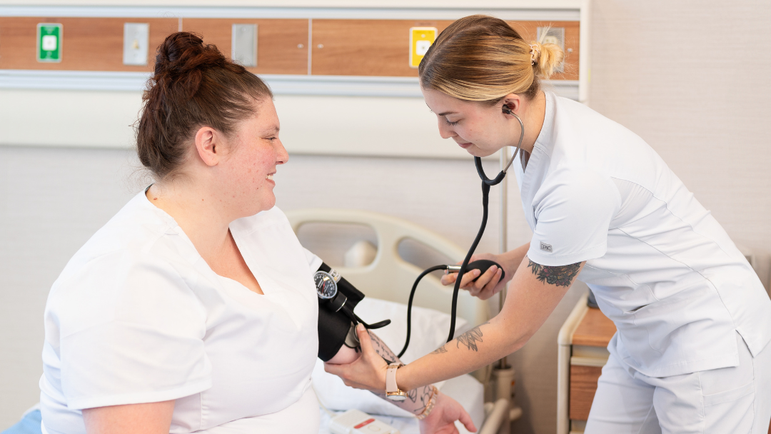 Pictured are two nurse aid students practicing blood pressure reading. 